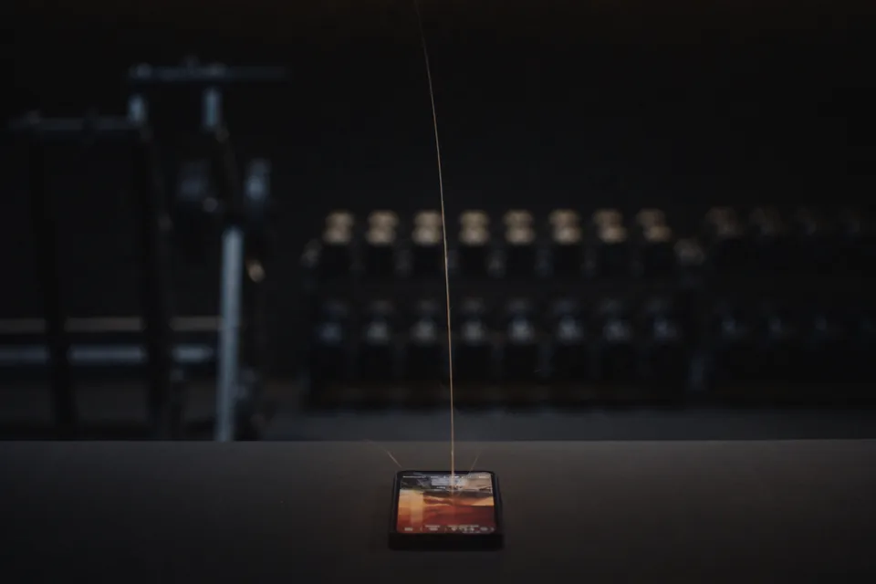 A phone on the front desk of a dark gym, dumbbell racks behind it, a thin thread of light rising from it